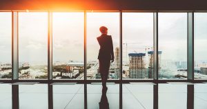 Silhouette businesswoman standing near full glass window and looking outside