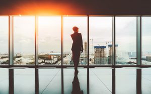 Silhouette businesswoman standing near full glass window and looking outside